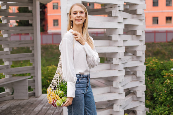 Young woman holding string shopping bag with fruits. Reusable eco bag for shopping. Zero waste, plastic free concept. Eco lifestyle. Eco shopping. Conscious consumption. Eco trend. Copy space - Photo, image