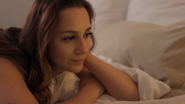 Young woman lies on the bed with her laptop and watches movies - Záběry, video