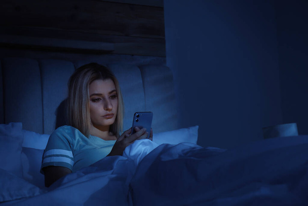Young woman using smartphone in bed at night. Nomophobia and sleeping disorder problem - Zdjęcie, obraz