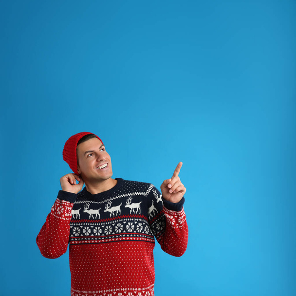Homme heureux en pull de Noël et chapeau sur fond bleu - Photo, image