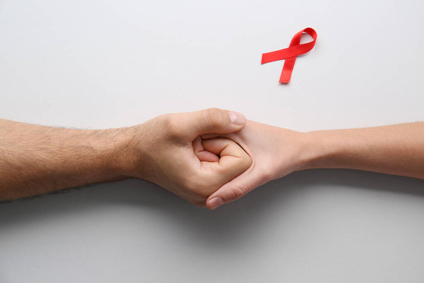 People holding hands near red awareness ribbon on white background, top view. World AIDS disease day - Фото, изображение