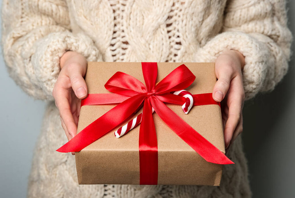 Woman holding Christmas gift box on grey background, closeup - Foto, Bild