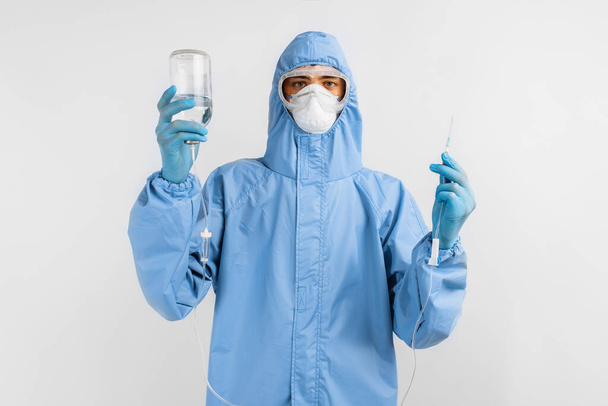 Doctor in protective medical suit, mask, goggles and gloves preparing the system for transfusion of infusion solutions, hospital and medical care concept, coronavirus, COVID-19 - Фото, изображение