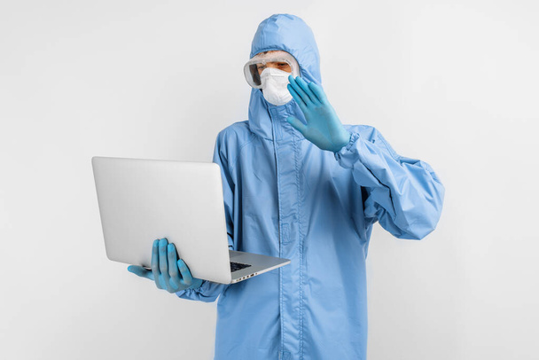 doctor in protective medical suit, mask, glasses and gloves working with laptop, giving patient advice on online service, on isolated white background, healthcare, disease prevention - 写真・画像