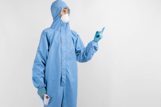 Male doctor wearing protective suit to protect against coronavirus, glasses, mask and gloves pointing to copy space on white background, coronavirus epidemic concept - Foto, afbeelding