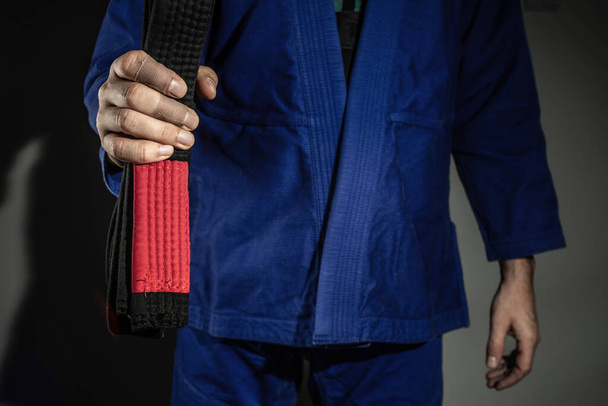 Zbliżenie na rękę nieznanego białego człowieka gospodarstwa brazylijski jiu jitsu bjj czarny pas podczas noszenia kimono gi w ciemnej siłowni - sztuki walki mistrzowskie umiejętności i koncepcja osiągnięcia pewności siebie - Zdjęcie, obraz