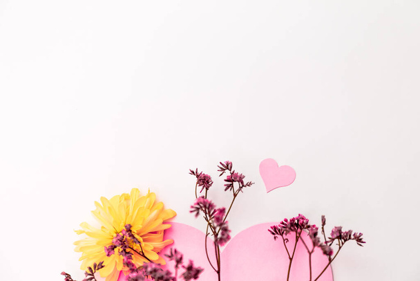 Küçük pembe çiçeklerle süslenmiş büyük pembe bir kalp ve beyaz bir zemin üzerinde sarı kasımpatılar, aşkın sembolü. - Fotoğraf, Görsel