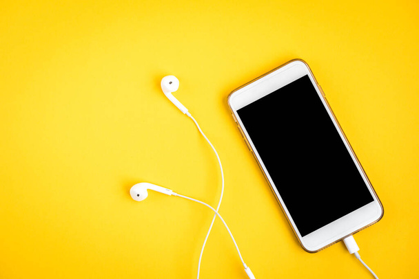 Mobile phone and headphones on yellow background - Foto, afbeelding