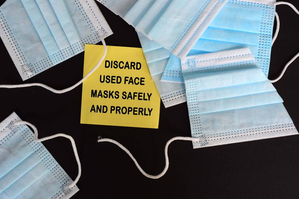黄色の付箋に書かれた使用済みフェイスマスクを処分するための警告とアドバイス。Covid-19 - 写真・画像