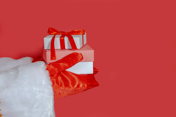 Santa Claus holds out his hands with gifts on a red isolated background. Close-up, selective focus, banner, copy space. The Concept Of A Happy Christmas. - Fotoğraf, Görsel