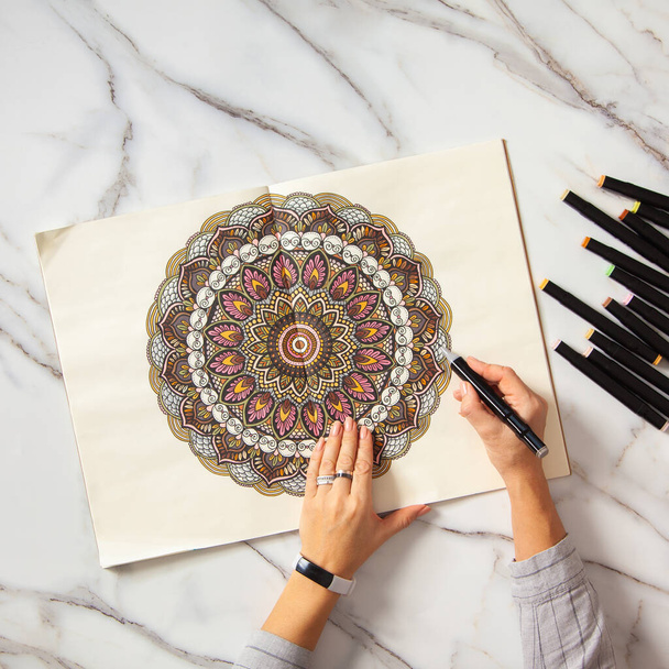 Woman drawing and coloring mandala in sketchbook with colorful markers while having breakfast with coffee and macarons on white marble table. Stress relieving trend by painting. Art therapy. Leisure. - Фото, зображення