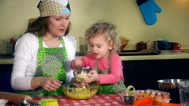 Pieni söpö auttaja tytär auttaa kaunista äitiä kakku leivontaan keittiössä - Materiaali, video