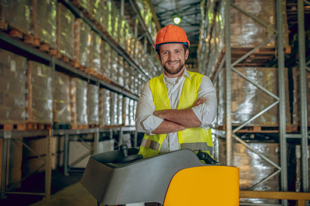 Warehouse worker in orange helmet looking contented - Фото, изображение
