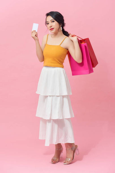 Teljes hossza gyönyörű fiatal ázsiai színes bevásárló táska és hitelkártya felett rózsaszín háttér. - Fotó, kép