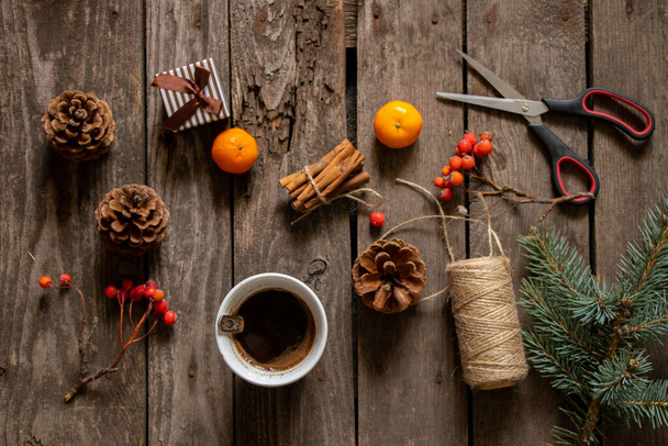 cup with coffee next to a branch of a christmas tree tangerine cinnamon on a wooden table, christmas table with coffee - Foto, afbeelding