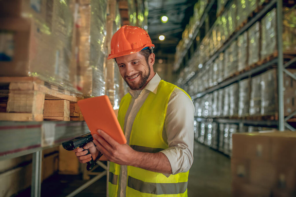 Warehouse worker in yellow vest looking at the tablet and smiling - Photo, Image