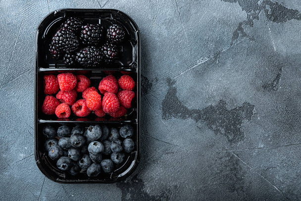 Ягодное блюдо, сбор ягод, черника, малина с ежевикой, вид сверху с копировальным пространством, на сером фоне - Фото, изображение