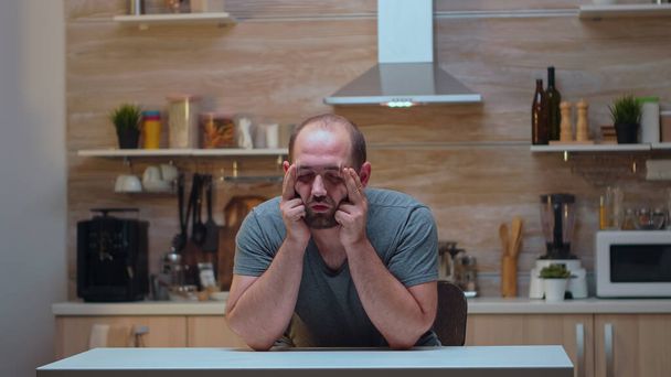 Ο άνθρωπος με πονοκεφάλους κάθεται στην κουζίνα - Φωτογραφία, εικόνα