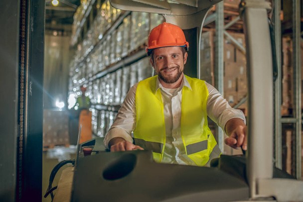 Young bearded worker sitting at the loader and smiling - Foto, Imagen