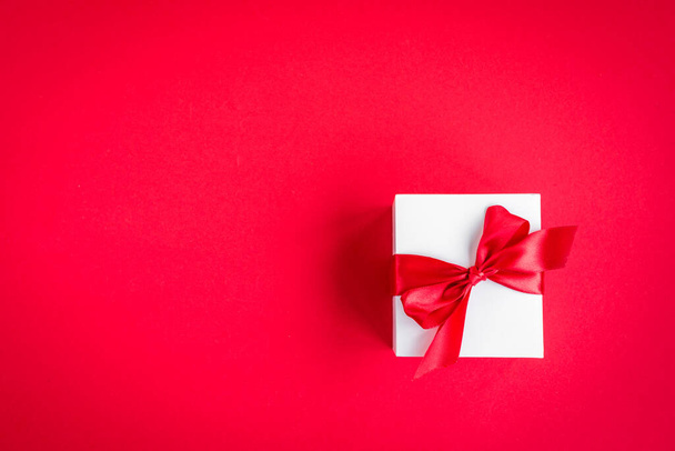 Geschenkkarton mit roter Schleife auf rotem Hintergrund. - Foto, Bild
