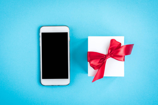 Mobiltelefon és ajándék doboz piros íj kék háttér. - Fotó, kép