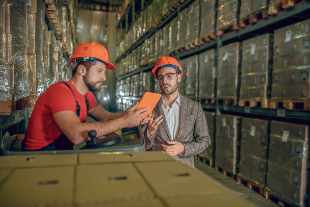 Warehouse worker showing data from internet to the warehouse manager - Foto, imagen
