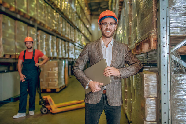 Warehouse manager in orange helmet holding a laptop - Foto, Bild