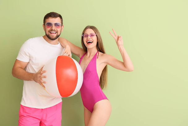 Νεαρό ζευγάρι με κομψά γυαλιά ηλίου και φουσκωτή μπάλα στο φόντο χρώμα - Φωτογραφία, εικόνα