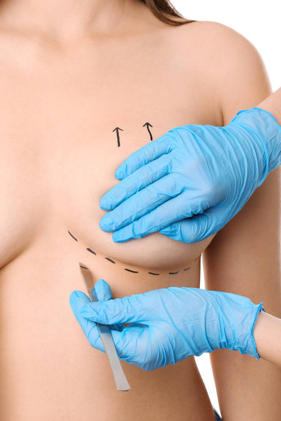 Woman and doctor with lancet on white background, closeup. Concept of breast augmentation - Φωτογραφία, εικόνα