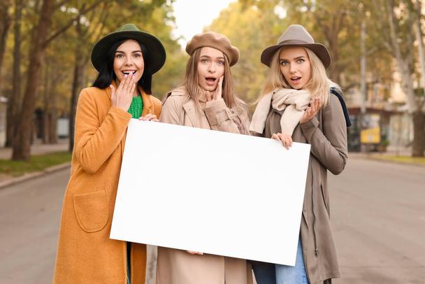 Beautiful surprised young women with blank poster outdoors - Fotografie, Obrázek