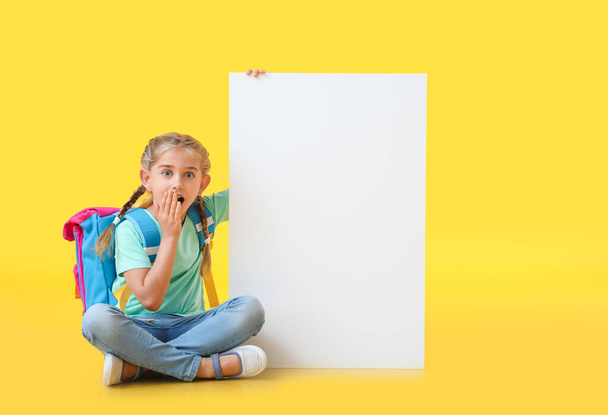 Surprised little schoolgirl with blank poster on color background - Photo, Image