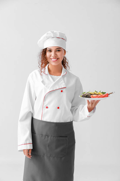 Young African-American female chef on light background - Foto, imagen