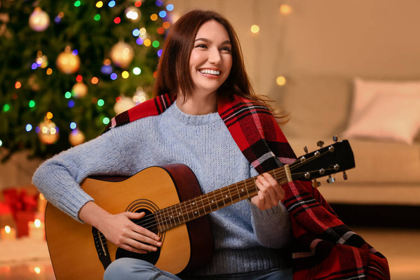 Belle jeune femme jouant de la guitare à la maison la veille de Noël - Photo, image