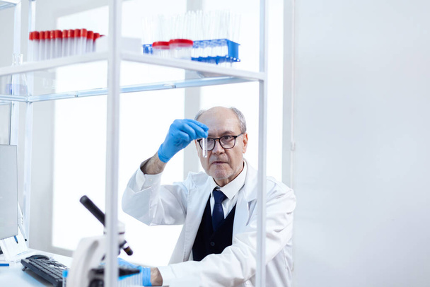 Άνδρας ανώτερος επιστήμονας στο ιατρικό εργαστήριο που εξετάζει δοκιμαστικό σωλήνα - Φωτογραφία, εικόνα