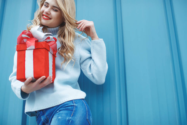 Счастливая молодая женщина с подарочной коробкой на синем фоне. - Фото, изображение