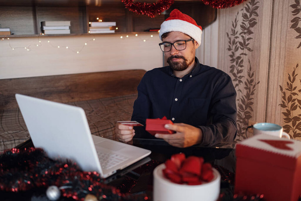 Happy man wearing Santa Claus hat . Buying christmas gifts online - online shopping concept. Ecommerce website xmas time holiday online shopping sale. - Фото, изображение