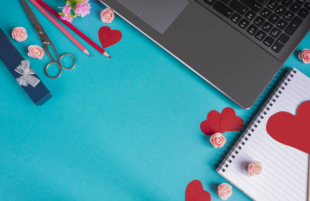 The background of Valentine's day. Empty blank Notepad, laptop, pencils, scissors, red hearts on a blue background. Valentine's day greeting card concept. Flat layout, top view, copy space - 写真・画像