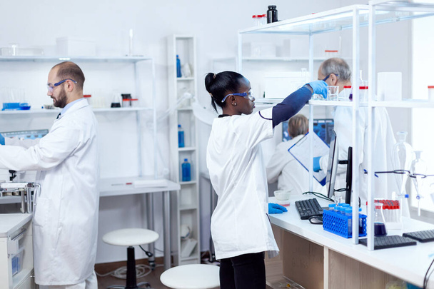 Afrikkalainen kemisti ammattimaisessa laboratoriossa ottamassa lasipulloa liuoksella - Valokuva, kuva