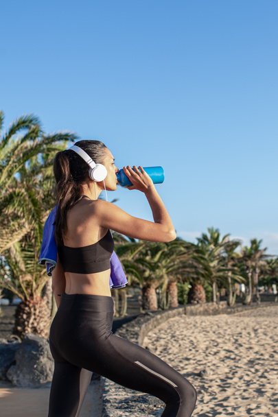 Beautiful fitness woman drinking water after training at the beach . - Photo, Image