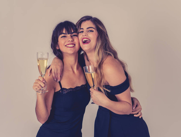 Two beautiful girlfriends having fun celebrating Christmas or New Year eve toasting glasses. Women posing in stylish sexy party dresses drinking champagne. People Friendship and Celebration. - Photo, image