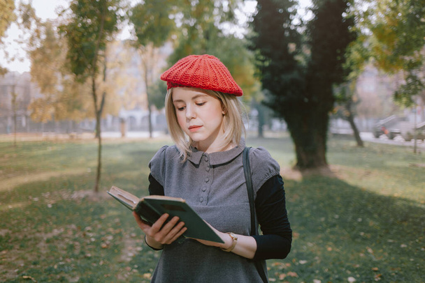 Young student reading a book at school campus. Woman with red beret at an european university in autumn. - Фото, изображение
