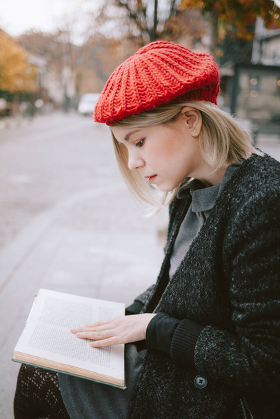 Young exchange student reading a book in the old town. European woman with red beret reading outdoors. - Fotó, kép