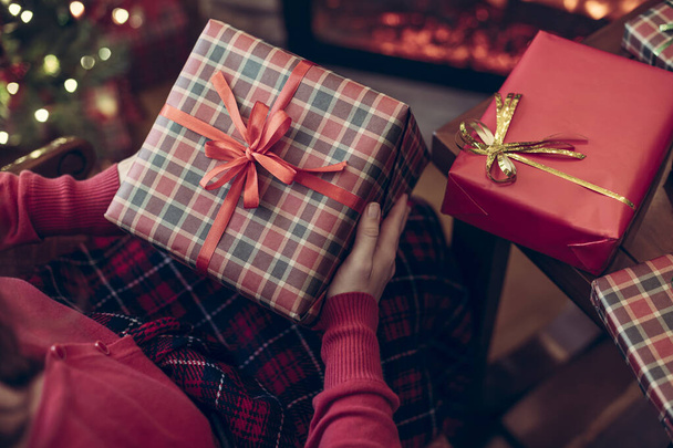 Woman holding huge gift box sitting near christmas tree and fireplace. Packing handmade christmas gifts .  - Фото, изображение