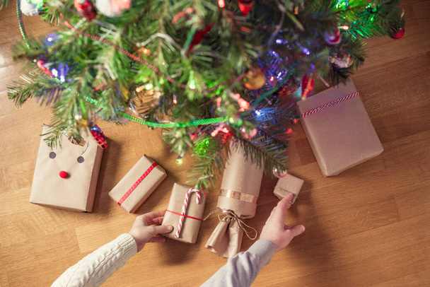 Woman and man putting hand made gift wrapping in a kraft paper under christmas tree. Presents for family. Top view. Flat lay. - Φωτογραφία, εικόνα
