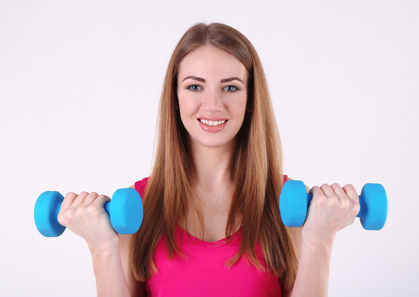 Young beautiful fitness girl exercising with dumbbells in gym - Foto, afbeelding