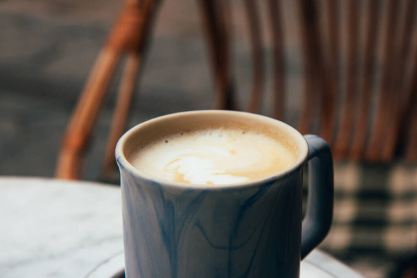 Xícara de cappuccino em uma bandeja de ferro em uma mesa em um café de rua, ao lado da cadeira de vime de mesa com uma xadrez xadrez. Foco seletivo. Fechar - Foto, Imagem