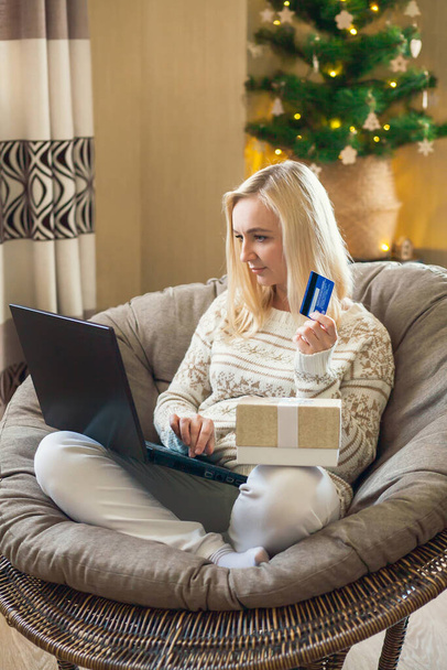 Las compras en línea de Navidad y de Año Nuevo - la mujer se sienta en la silla redonda y paga por las compras en línea con tarjeta de crédito usando el ordenador portátil. - Foto, imagen