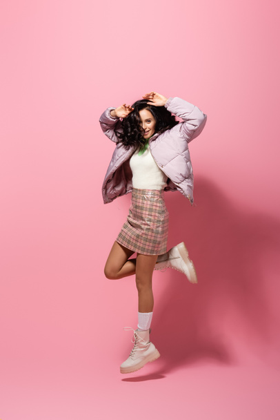 brunette young woman in stylish winter outfit jumping on pink background - Foto, Imagem