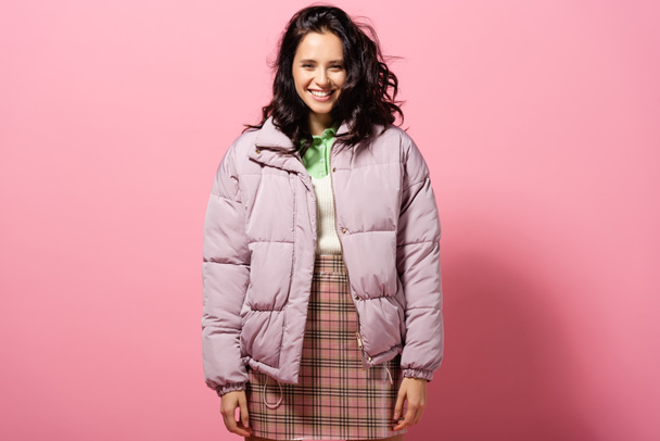 smiling brunette young woman in puffer jacket on pink background - Photo, Image