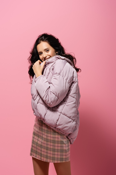 smiling brunette young woman in puffer jacket posing on pink background - Fotografie, Obrázek
